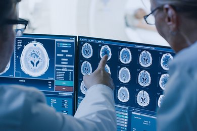 zwei medizinische Fachpersonen schauen auf einen Monitor mit Bilder eines Gehirnscans.